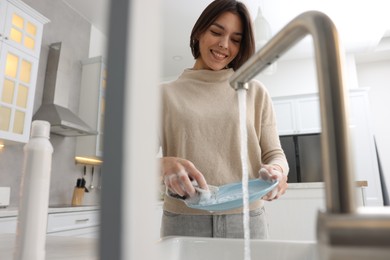 Photo of Happy woman washing plate above sink in modern kitchen, low angle view