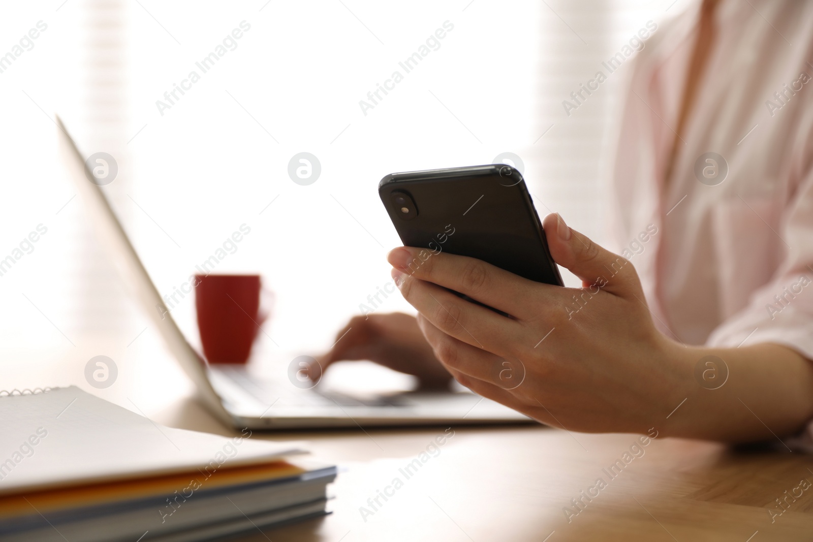 Photo of Woman with smartphone and laptop at table indoors, closeup