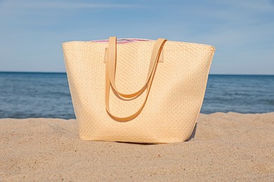 Photo of Stylish summer bag on sand near sea. Beach accessory