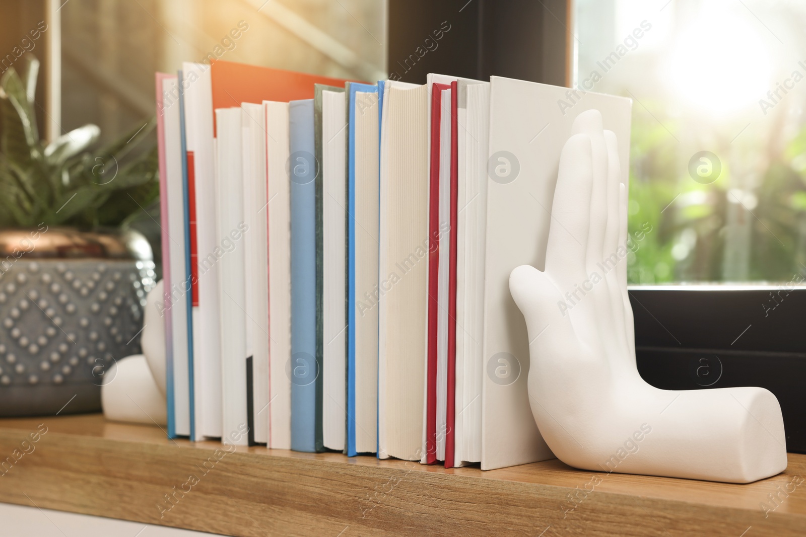 Photo of Beautiful hand shaped bookends with books on window sill indoors