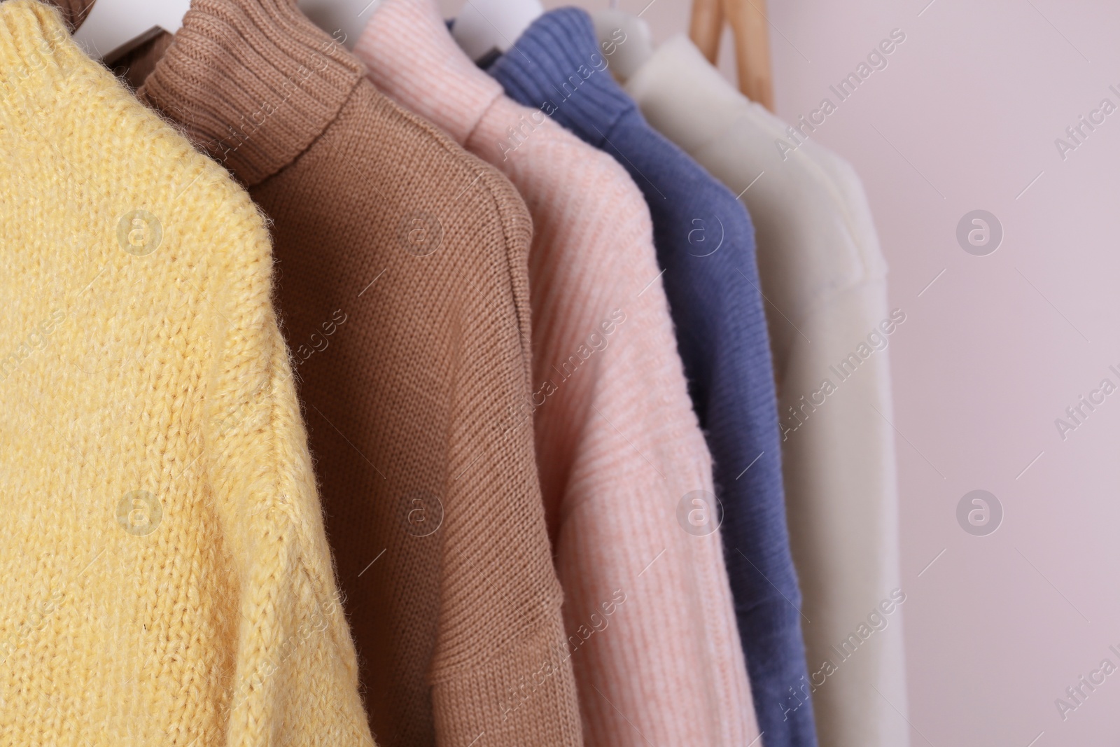 Photo of Warm sweaters hanging on wooden rack against light background, closeup