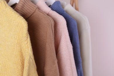 Warm sweaters hanging on wooden rack against light background, closeup