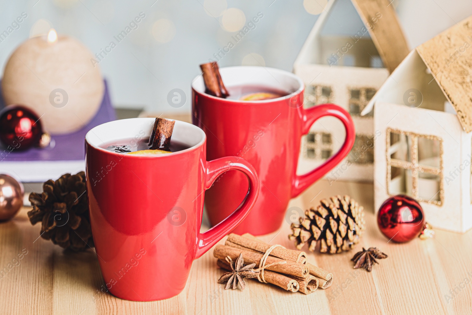 Photo of Cups of hot winter drink and Christmas decoration on wooden table against blurred lights