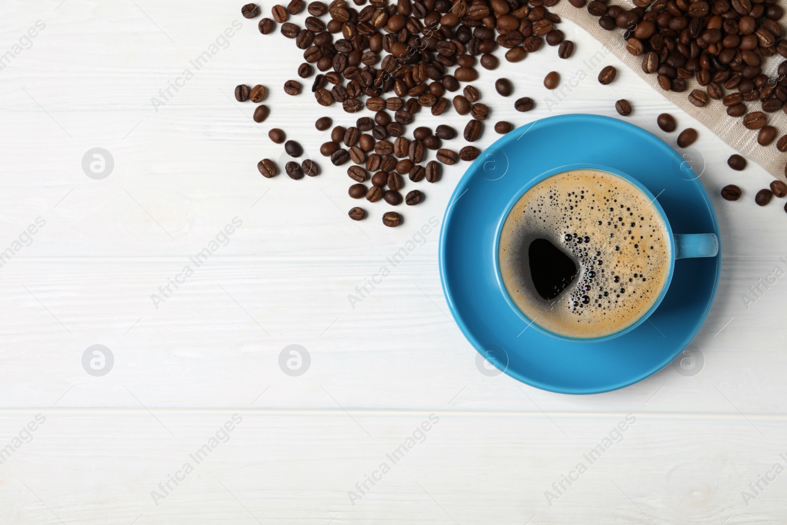 Photo of Cup of aromatic hot coffee and beans on white wooden table, flat lay. Space for text