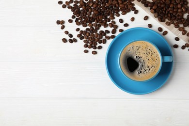 Photo of Cup of aromatic hot coffee and beans on white wooden table, flat lay. Space for text