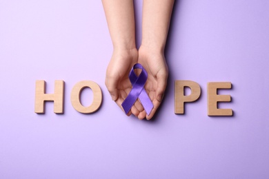 Woman with purple awareness ribbon and word HOPE made of wooden letters on violet background, top view