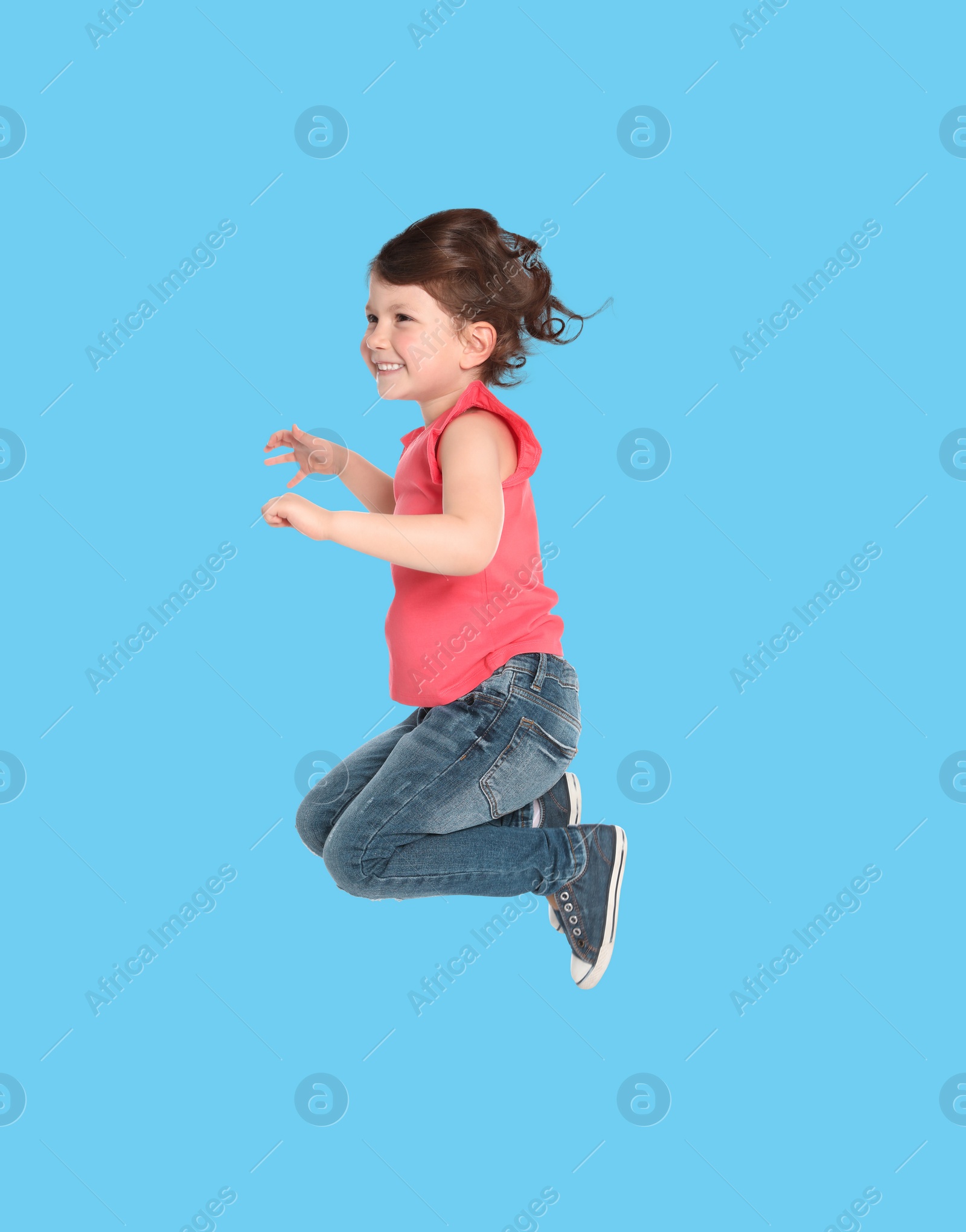 Image of Happy cute girl jumping on light blue background