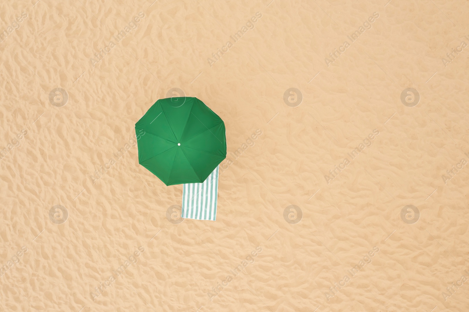 Image of Green beach umbrella and towel on sandy coast, aerial view. Space for text