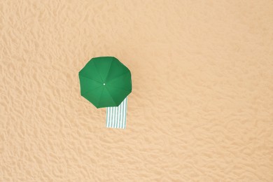 Green beach umbrella and towel on sandy coast, aerial view. Space for text