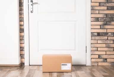 Photo of Cardboard parcel box on floor near apartment entrance. Mockup for design