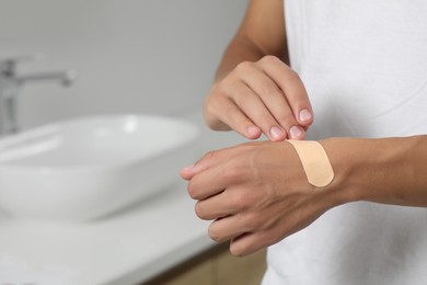 Photo of Man putting sticking plaster onto hand indoors, closeup. Space for text
