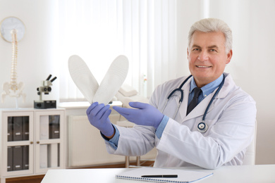 Photo of Senior male orthopedist showing insoles in clinic