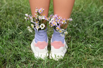 Photo of Woman with beautiful tender flowers in socks on green grass, closeup