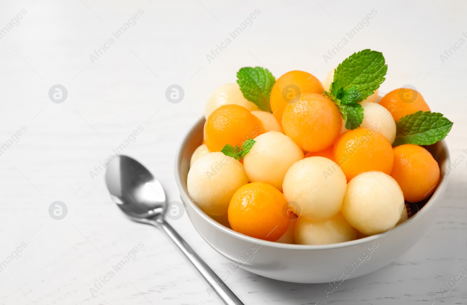 Photo of Melon balls and mint in bowl on white wooden table, closeup