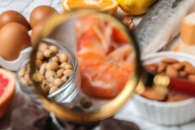 Photo of Different products with magnifier focused on shrimps and soy beans, closeup. Food allergy concept