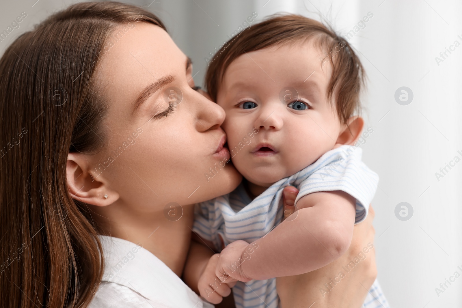 Photo of Happy mother kissing her little baby indoors, closeup