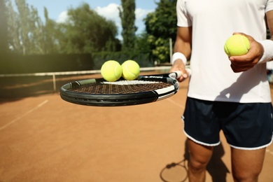 Sportsman with racket and tennis balls at court, closeup