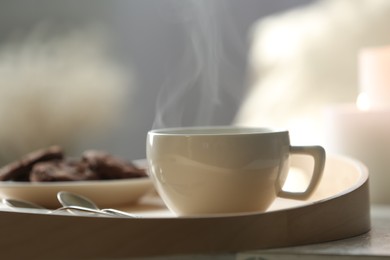 Cup of hot drink on wooden tray against blurred background, closeup