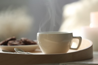 Photo of Cup of hot drink on wooden tray against blurred background, closeup