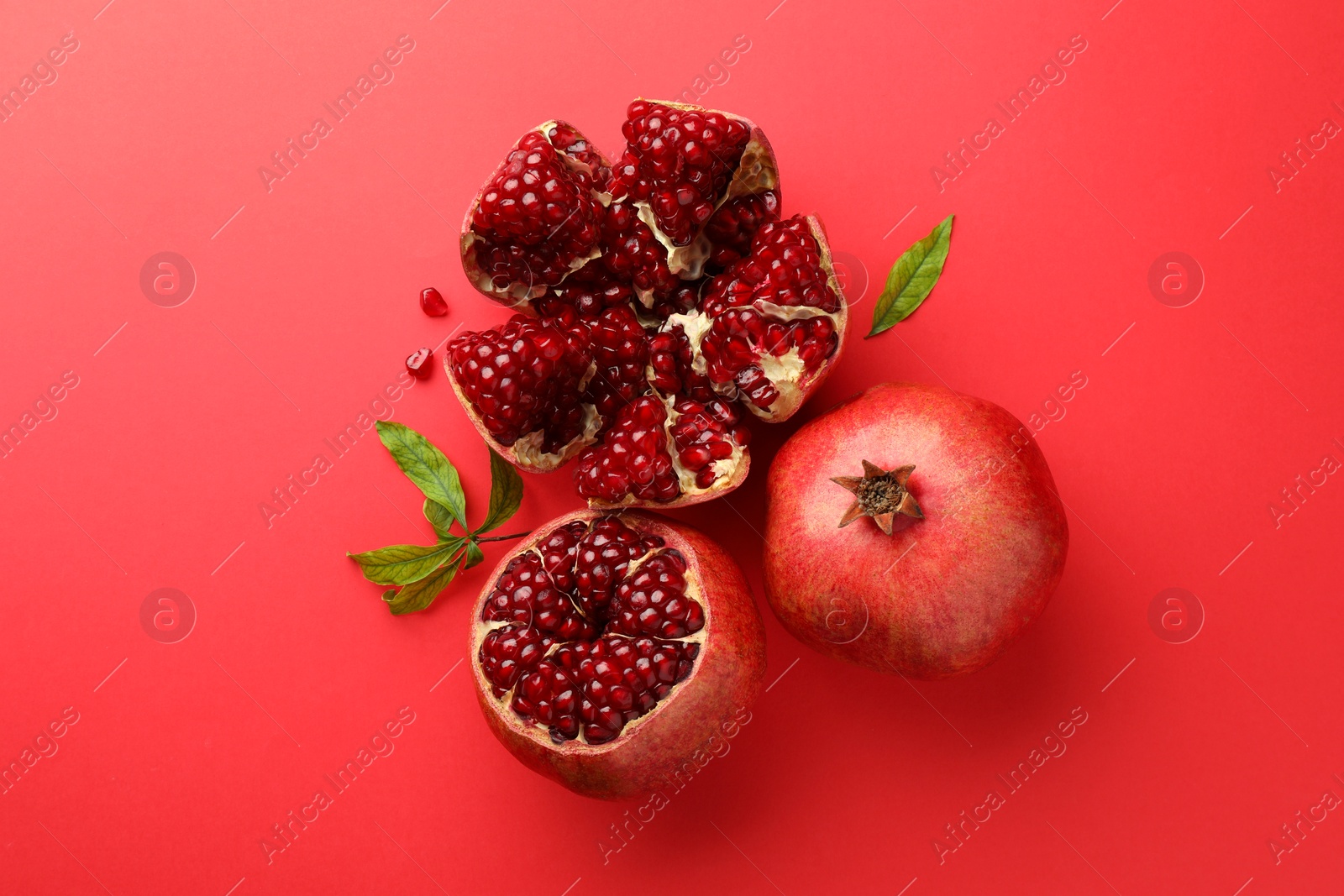Photo of Fresh pomegranates and green leaves on red background, flat lay
