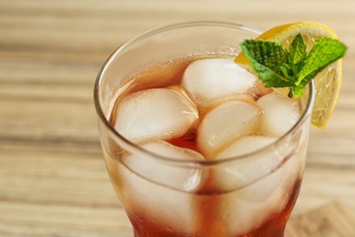 Photo of Glass of tasty ice tea with lemon and mint on wooden table, closeup
