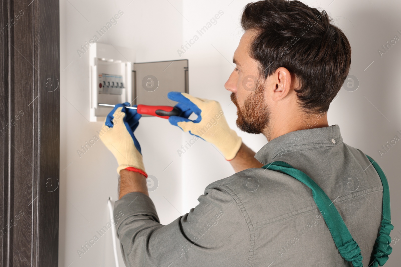 Photo of Electrician installing fuse box with screwdriver indoors