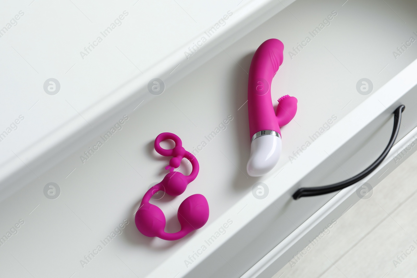 Photo of Modern vibrator and anal balls in open white drawer, above view. Sex toys