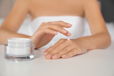 Photo of Woman applying moisturizing cream at white table, closeup
