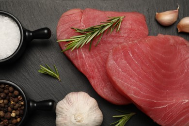 Fresh raw tuna fillets with rosemary and spices on black table, flat lay