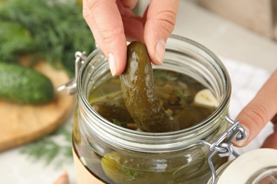 Woman taking pickled cucumber from jar at table, closeup view