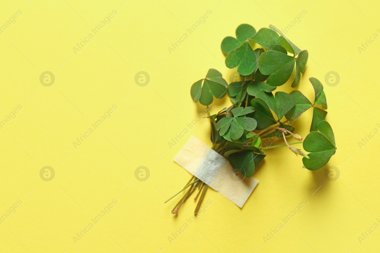 Photo of Bunch of green clover with tape on yellow background. Space for text