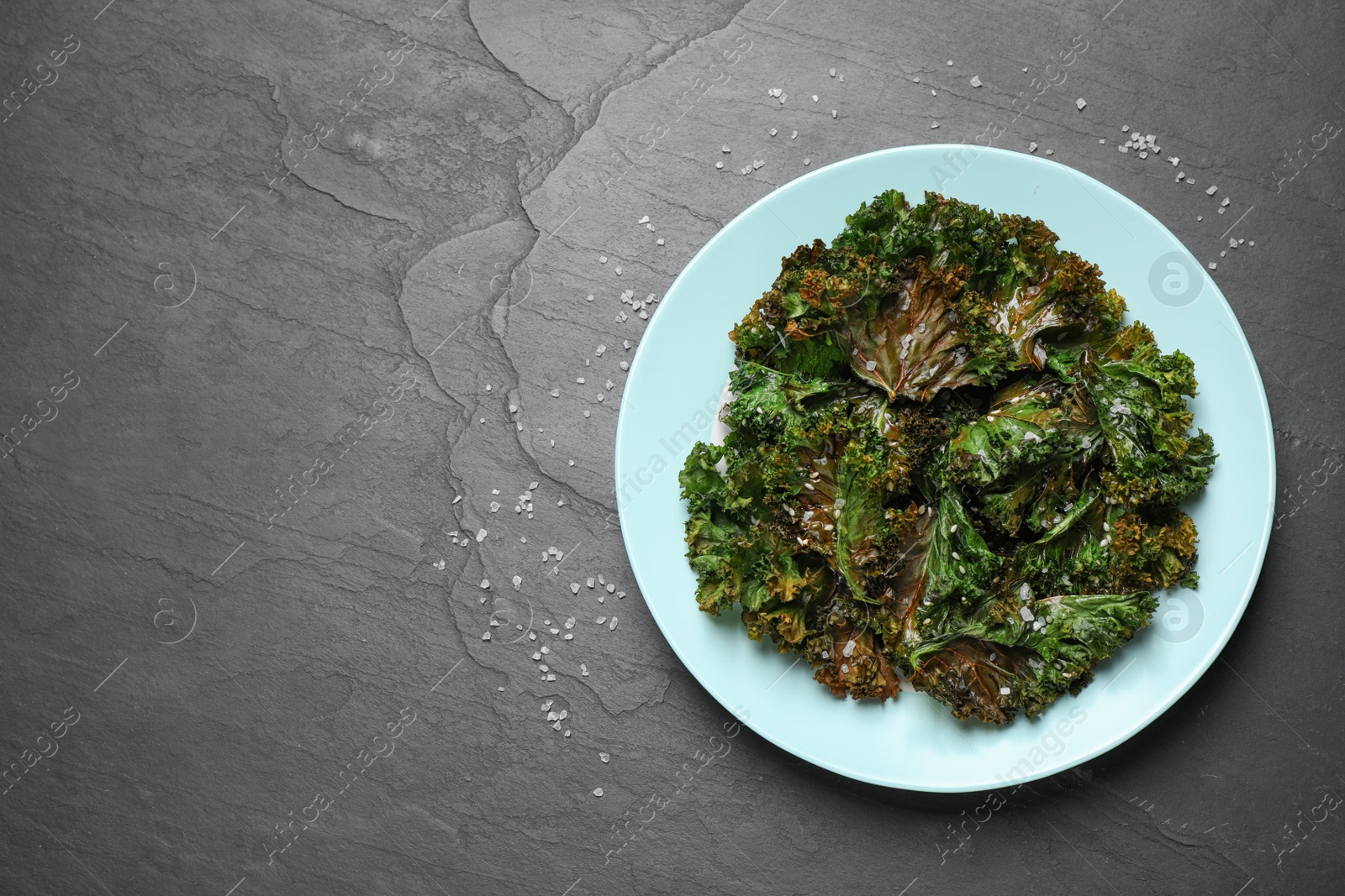 Photo of Tasty baked kale chips on dark grey table, top view. Space for text