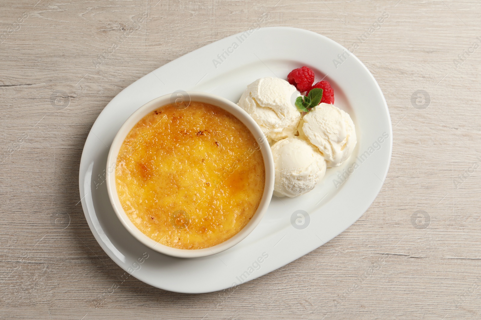 Photo of Delicious creme brulee served with scoops of ice cream, fresh raspberries and mint on light wooden table, top view