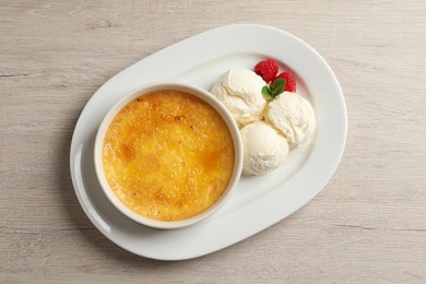 Photo of Delicious creme brulee served with scoops of ice cream, fresh raspberries and mint on light wooden table, top view