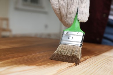 Photo of Man applying wood stain onto wooden surface against blurred background, closeup. Space for text