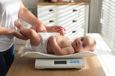 Photo of Young woman weighting her cute baby at home, closeup. Health care
