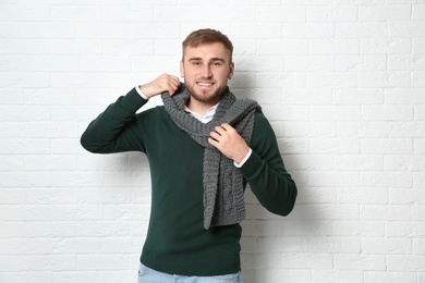 Handsome young man in warm sweater with scarf near white brick wall