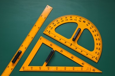 Photo of Protractor, triangle and ruler on green chalkboard, flat lay