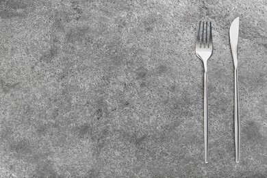 Photo of Shiny fork and knife on grey table, flat lay. Space for text