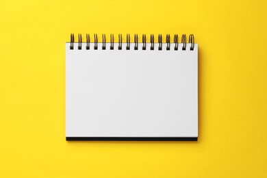 Photo of Spiral bound notebook on yellow background, top view