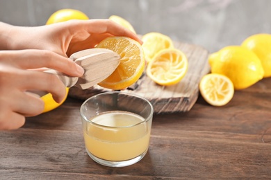 Photo of Young woman squeezing lemon juice with reamer into glass on table