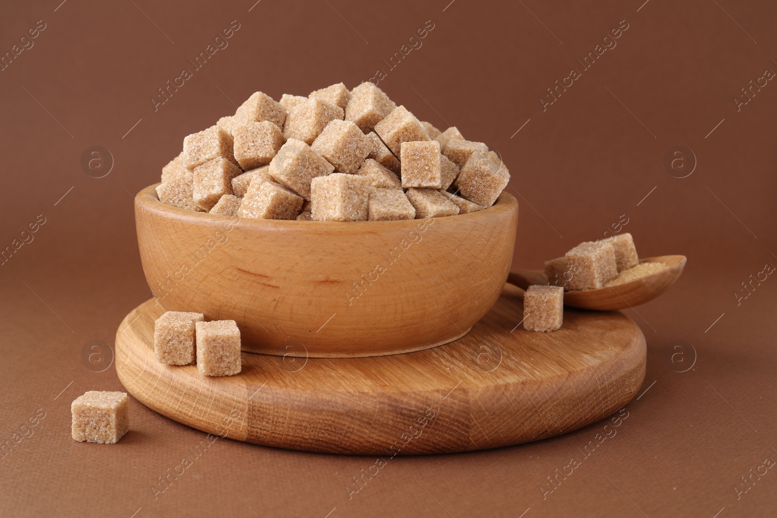 Photo of Brown sugar cubes in bowl and spoon on color background