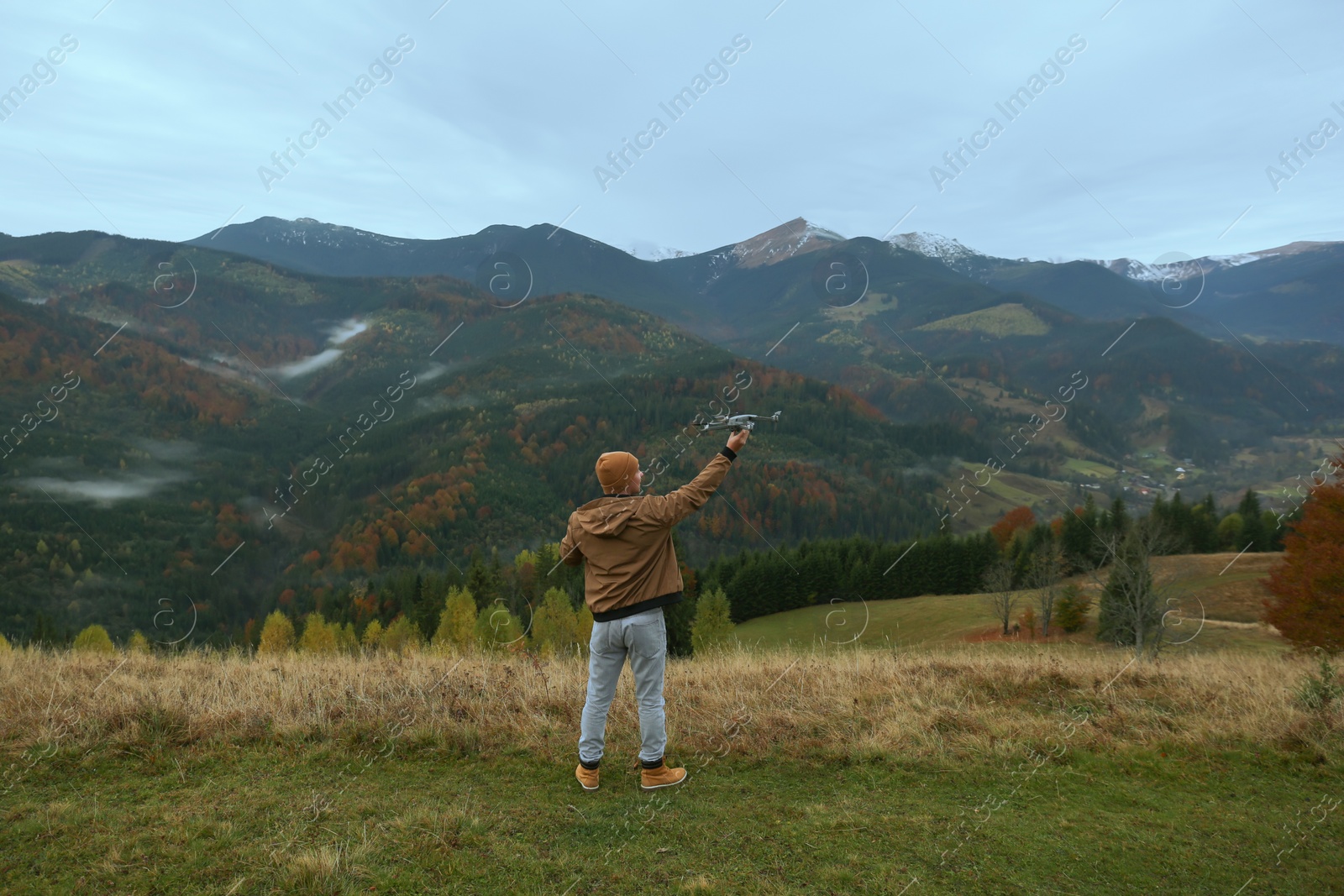 Photo of Young man with modern drone in mountains, back view