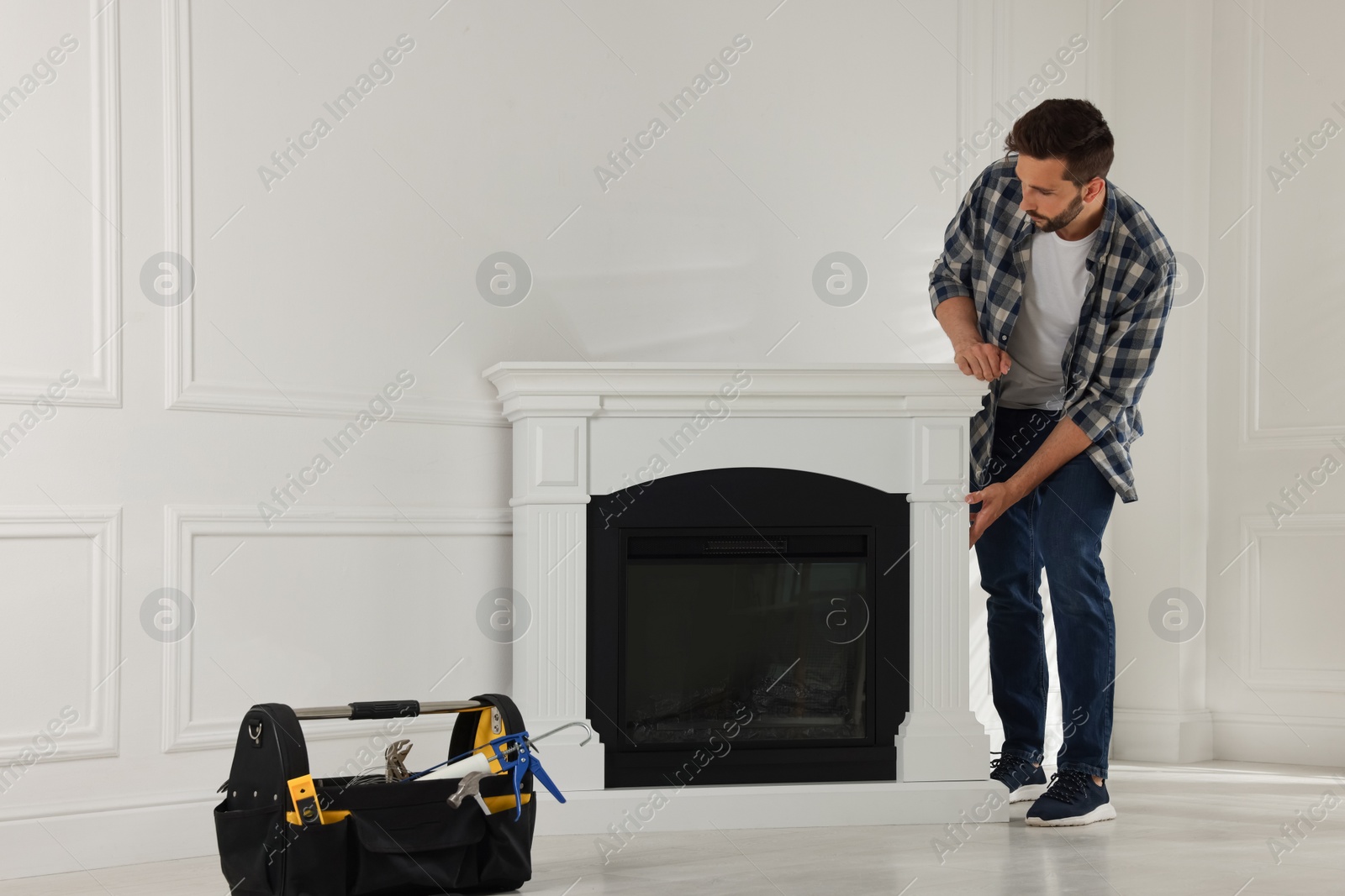 Photo of Man installing electric fireplace near white wall in room