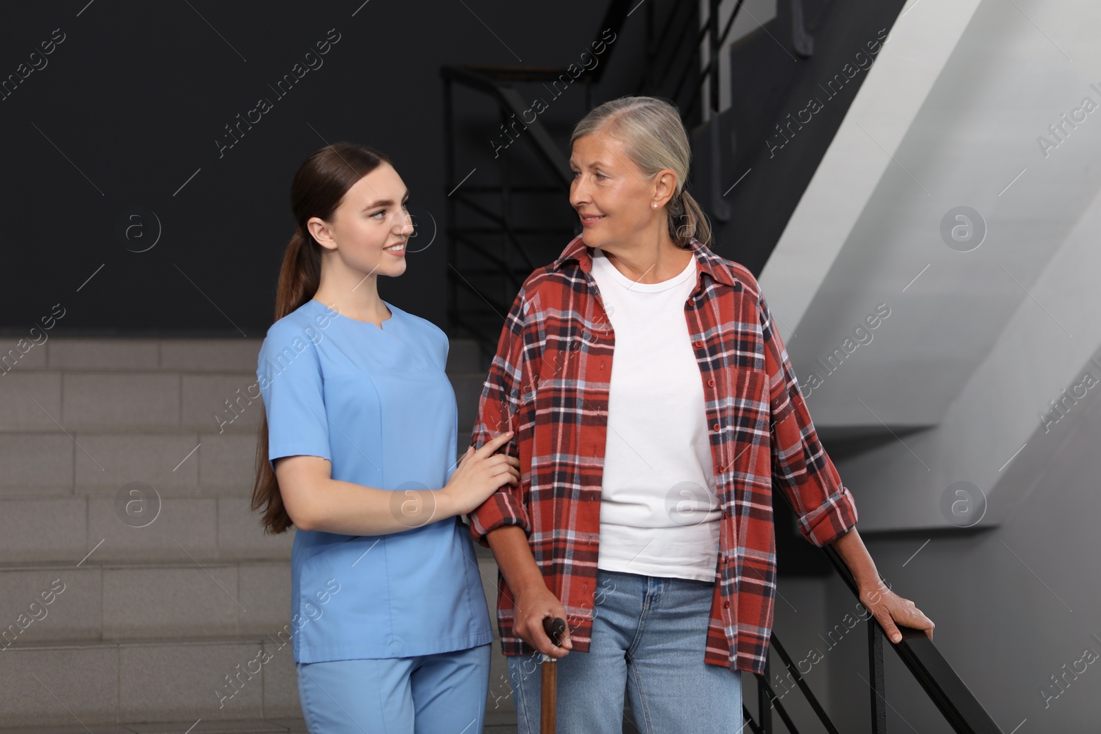 Photo of Young healthcare worker assisting senior woman on stairs indoors