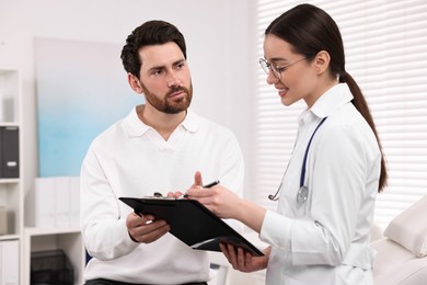 Photo of Doctor with clipboard consulting patient during appointment in clinic