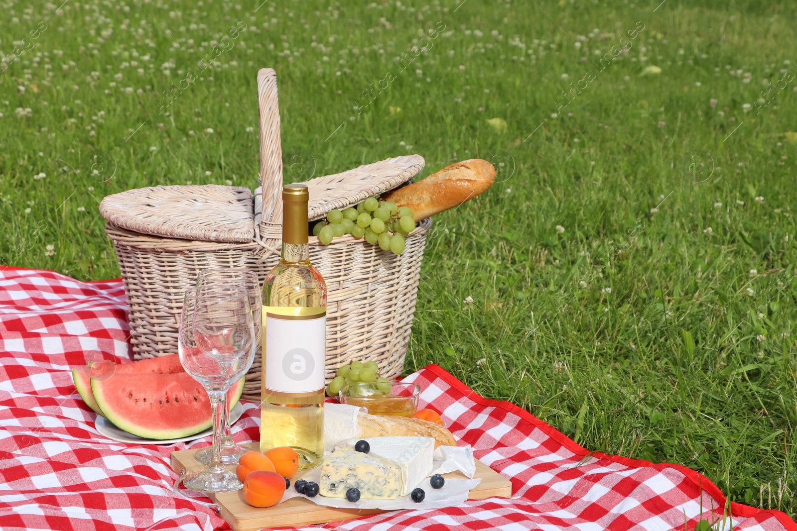 Photo of Picnic blanket with delicious food and wine outdoors on summer day