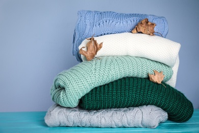 Photo of Stack of folded knitted sweaters and autumn leaves on blue wooden table against grey background