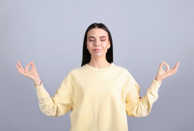 Photo of Young woman meditating on grey background. Stress relief exercise