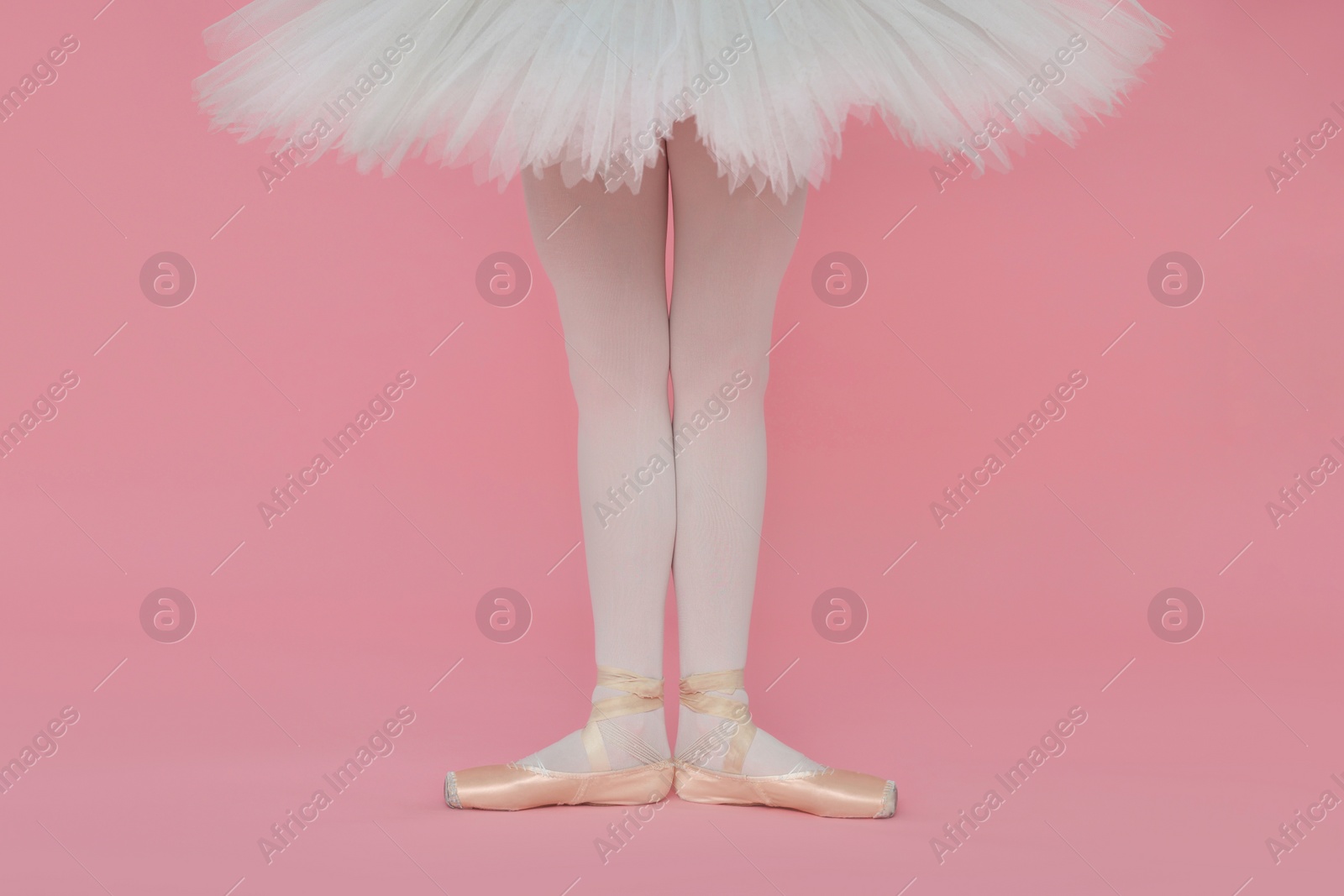 Photo of Young ballerina in pointe shoes practicing dance moves on pink background, closeup. Space for text